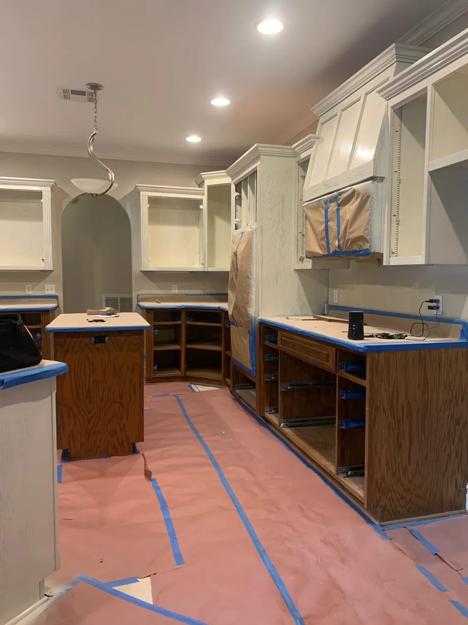 Kitchen cabinet painting in progress with floors covered, counters taped, and hardware removed