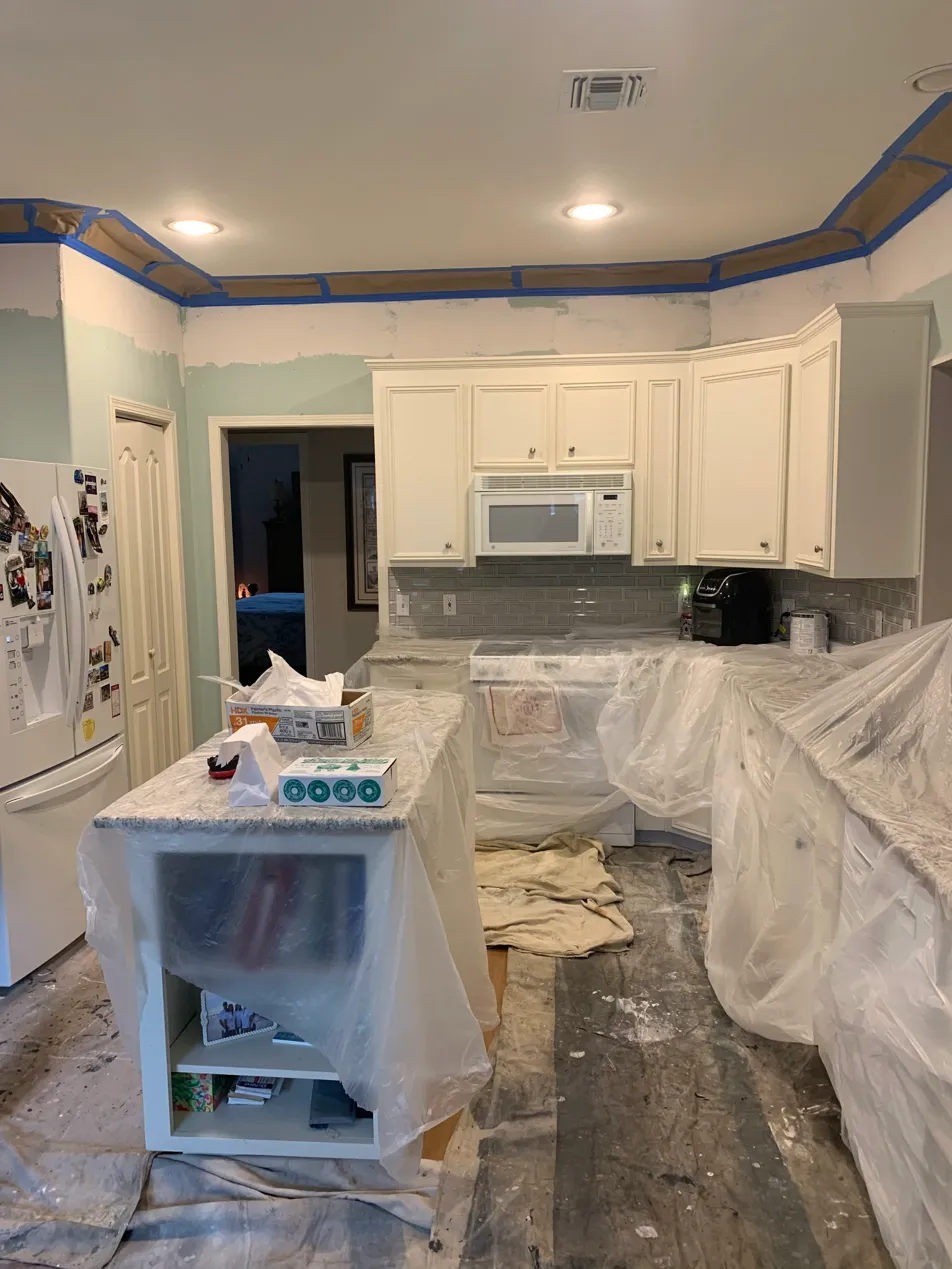 Kitchen interior painting in progress — wallpaper removed, counters covered, ceiling taped